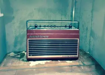 Vintage Schaub-Lorenz radio with a red and silver design, featuring buttons and a transparent cover, set in a worn room with peeling paint.