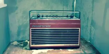 Vintage Schaub-Lorenz radio with a red and silver design, featuring buttons and a transparent cover, set in a worn room with peeling paint.