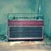 Vintage Schaub-Lorenz radio with a red and silver design, featuring buttons and a transparent cover, set in a worn room with peeling paint.