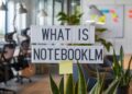 Office space with a sign reading "What is NotebookLM" above plants and desks, with sticky notes on a distant whiteboard.