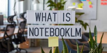 Office space with a sign reading "What is NotebookLM" above plants and desks, with sticky notes on a distant whiteboard.