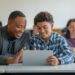 A teacher and student smile while looking at a tablet displaying an AI rubric generator in a classroom setting, with other students engaged in learning activities in the background.